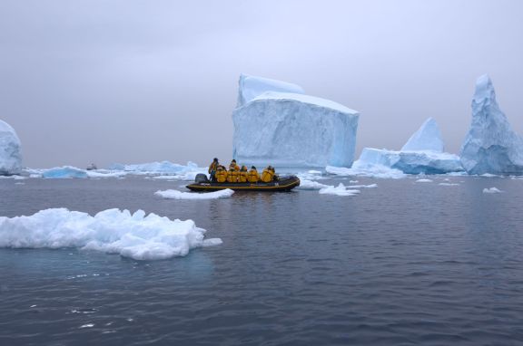 An expedition group in a boat navigating icy waters near giant icebergs in Antarctica.